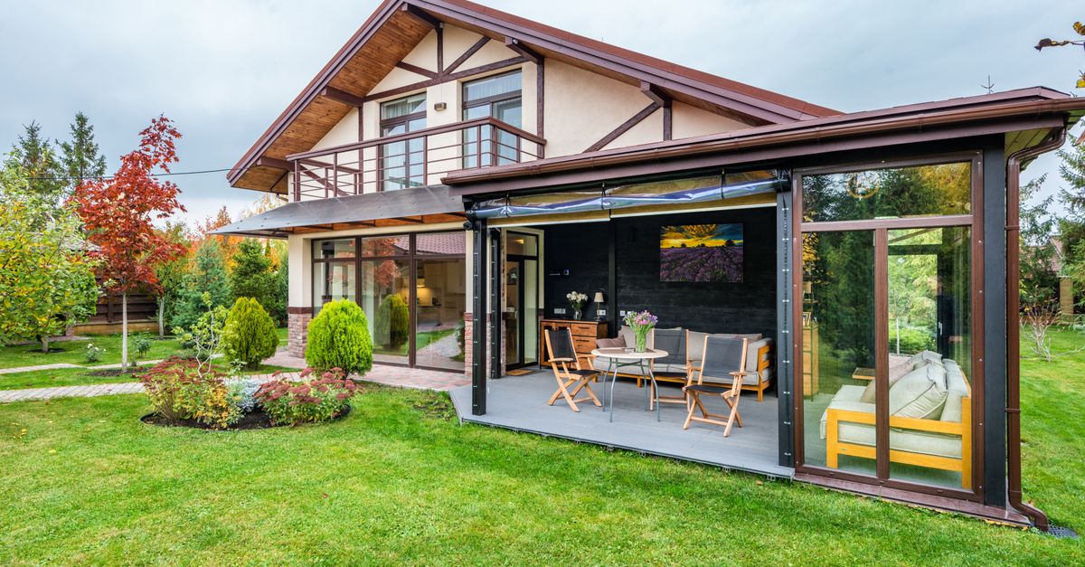 Residential cottage with balcony and opened veranda opening view on lawn and trees growing in backyard